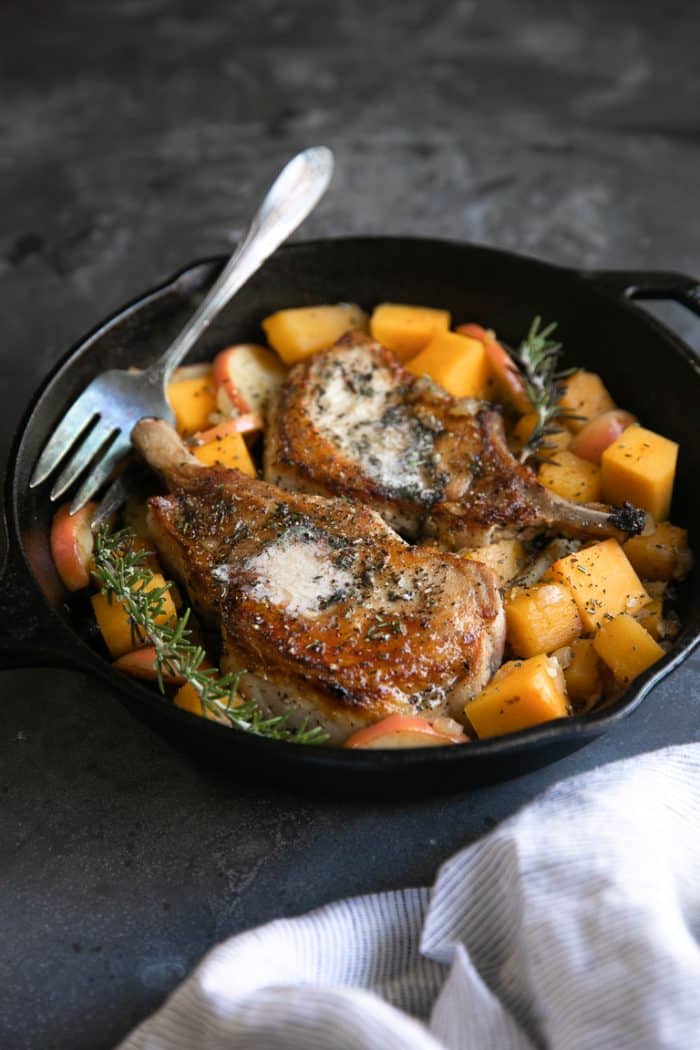 Angle view of bone-in pork chops in a cast-iron skillet with butternut squash and apples