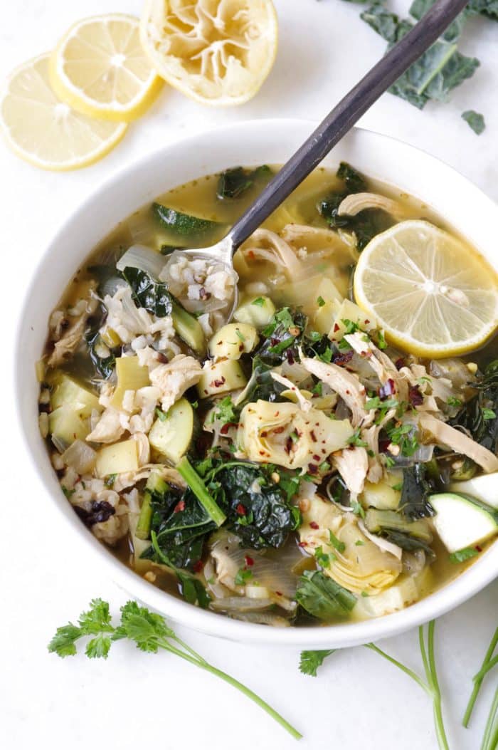Soup bowl filled with chicken, kale, and rice soup garnished with fresh lemon wedges.
