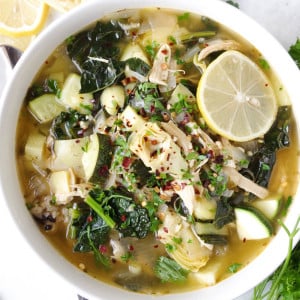Soup bowl filled with chicken, kale, and rice soup garnished with fresh lemon wedges.