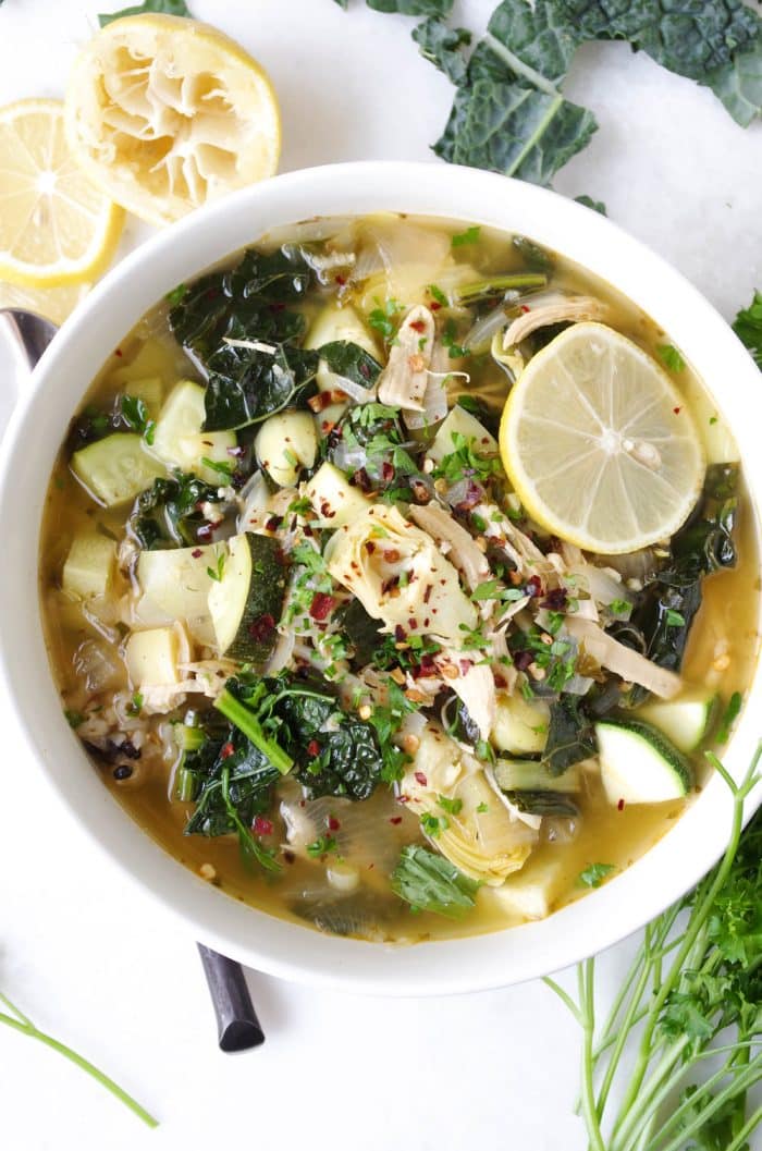 Soup bowl filled with chicken, kale, and rice soup garnished with fresh lemon wedges.