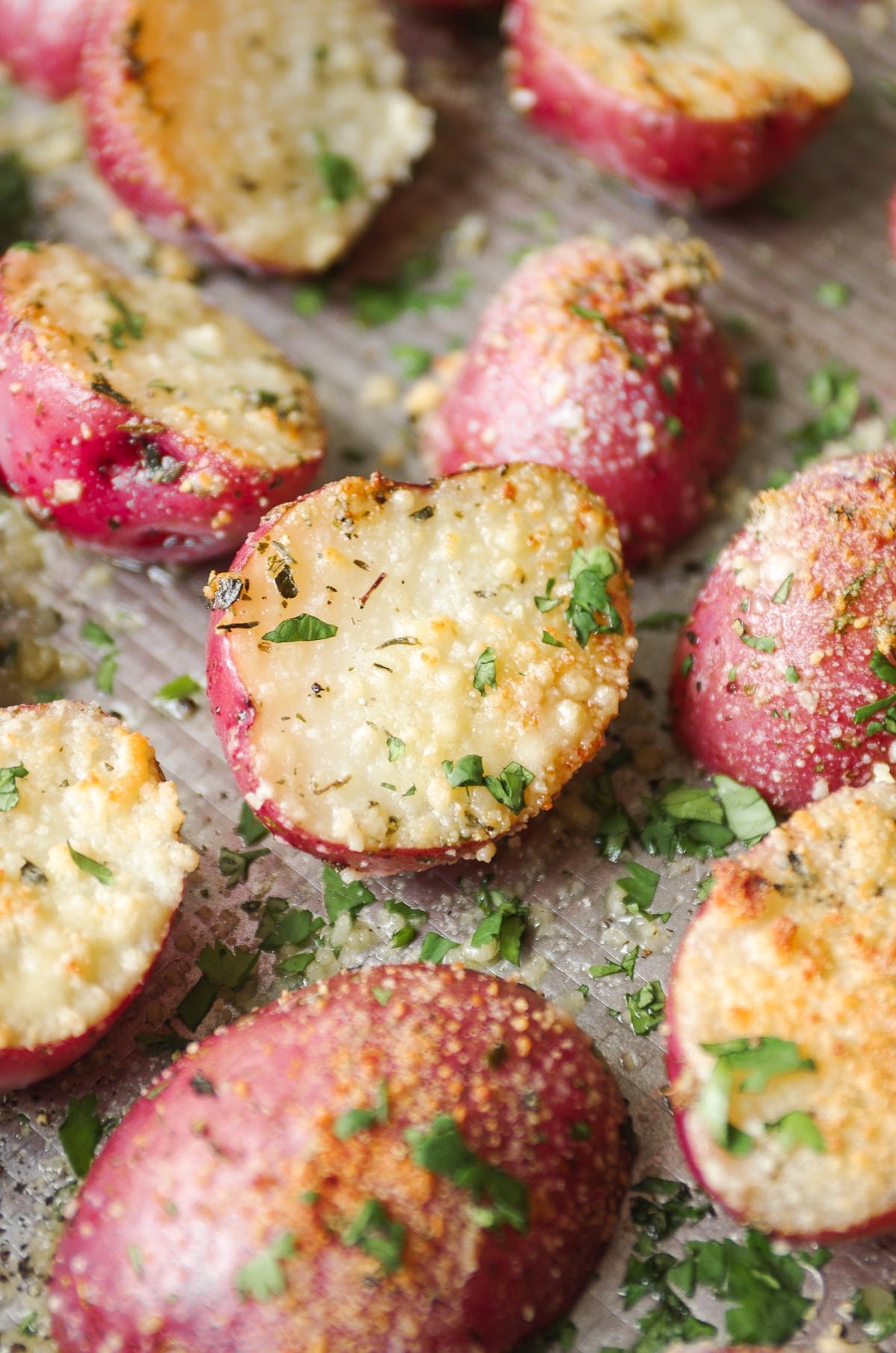 Close up image of halved roasted mini red potatoes that have been roasted with garlic, parmesan cheese, and herbs.