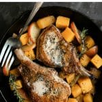 Skillet with two bone-in pork chops cooked with diced apples, butternut squash, and fresh herbs.