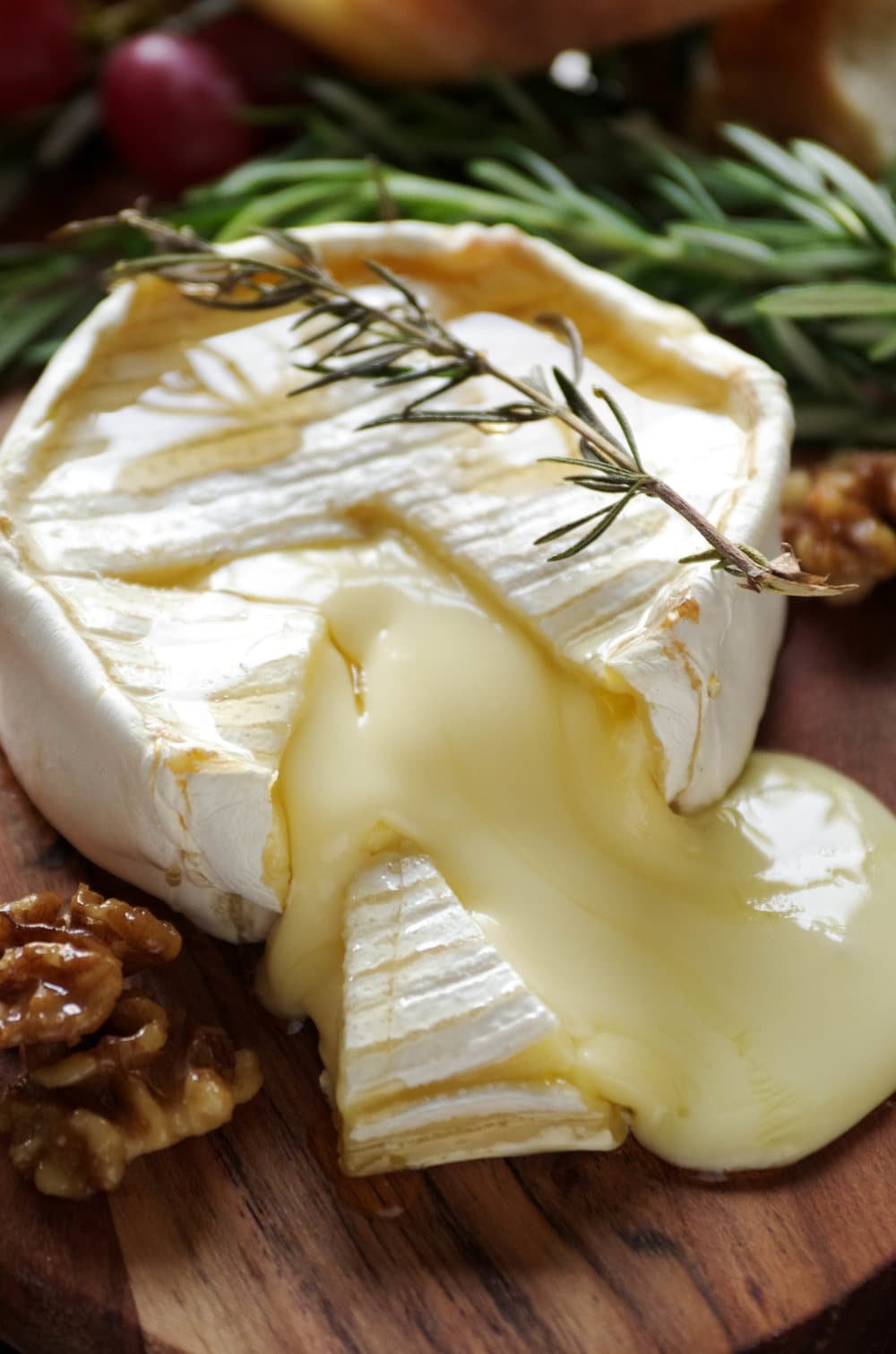 Block of baked brie on a small wood serving board sliced open with gooey cheese oozing out.
