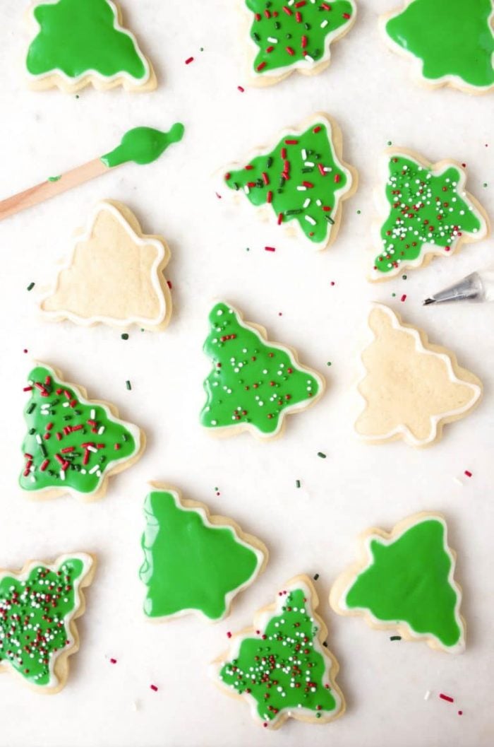 Decorated and undecorated sugar cookie cut-outs with glossy green frosting and Christmas colored sprinkles.