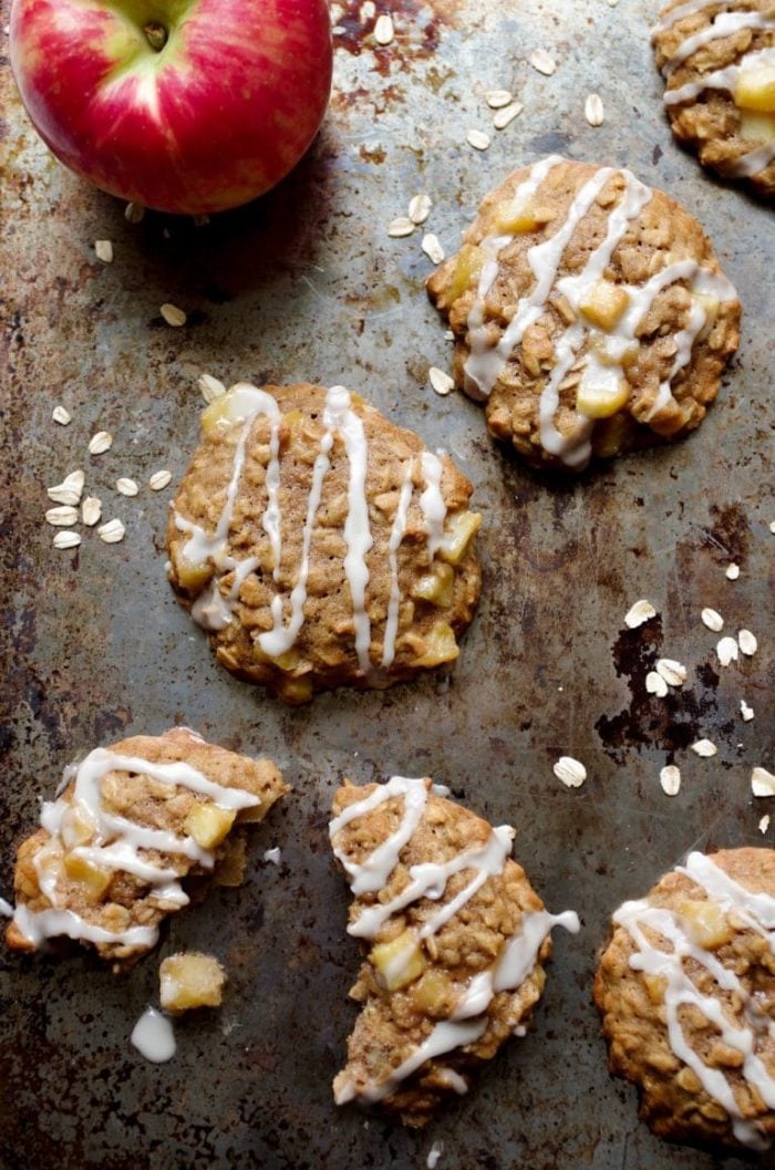 Oatmeal cookies filled with fried apples and drizzled with a sweet sugar glaze on a large baking sheet.