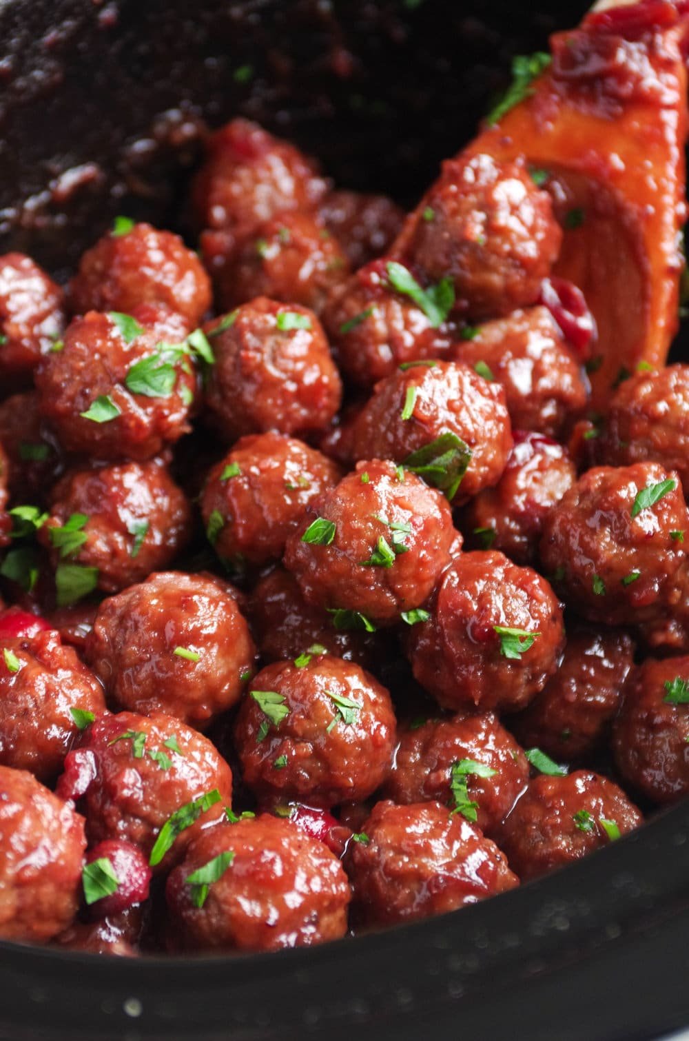 Cooked party meatballs in a large slow cooker covered with cranberry sauce.