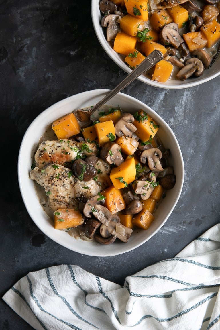 Two white bowls filled with cooked chicken, butternut squash, and mushrooms in a light cream sauce.