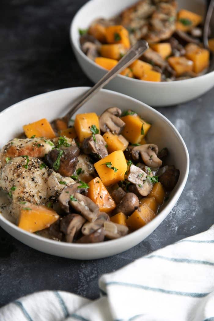 Two white bowls filled with cooked chicken, butternut squash, and mushrooms in a light cream sauce.