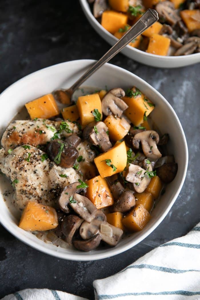 Two white bowls filled with cooked chicken, butternut squash, and mushrooms in a light cream sauce.