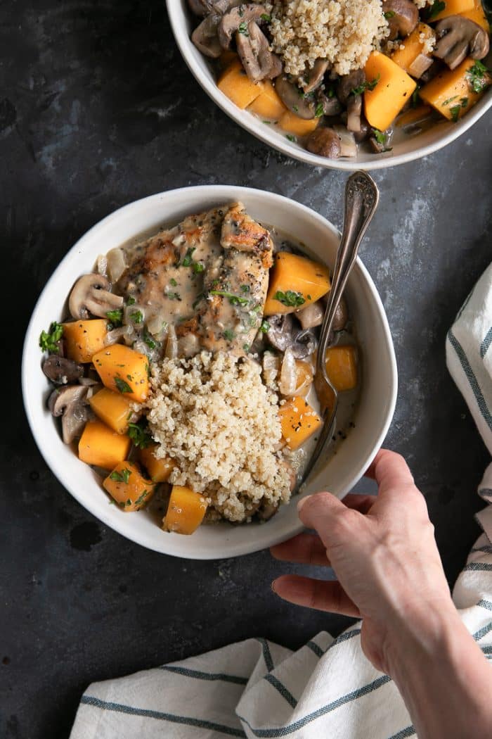 Two white bowls filled with cooked chicken, butternut squash, and mushrooms in a light cream sauce and topped with a scoop of cooked quinoa