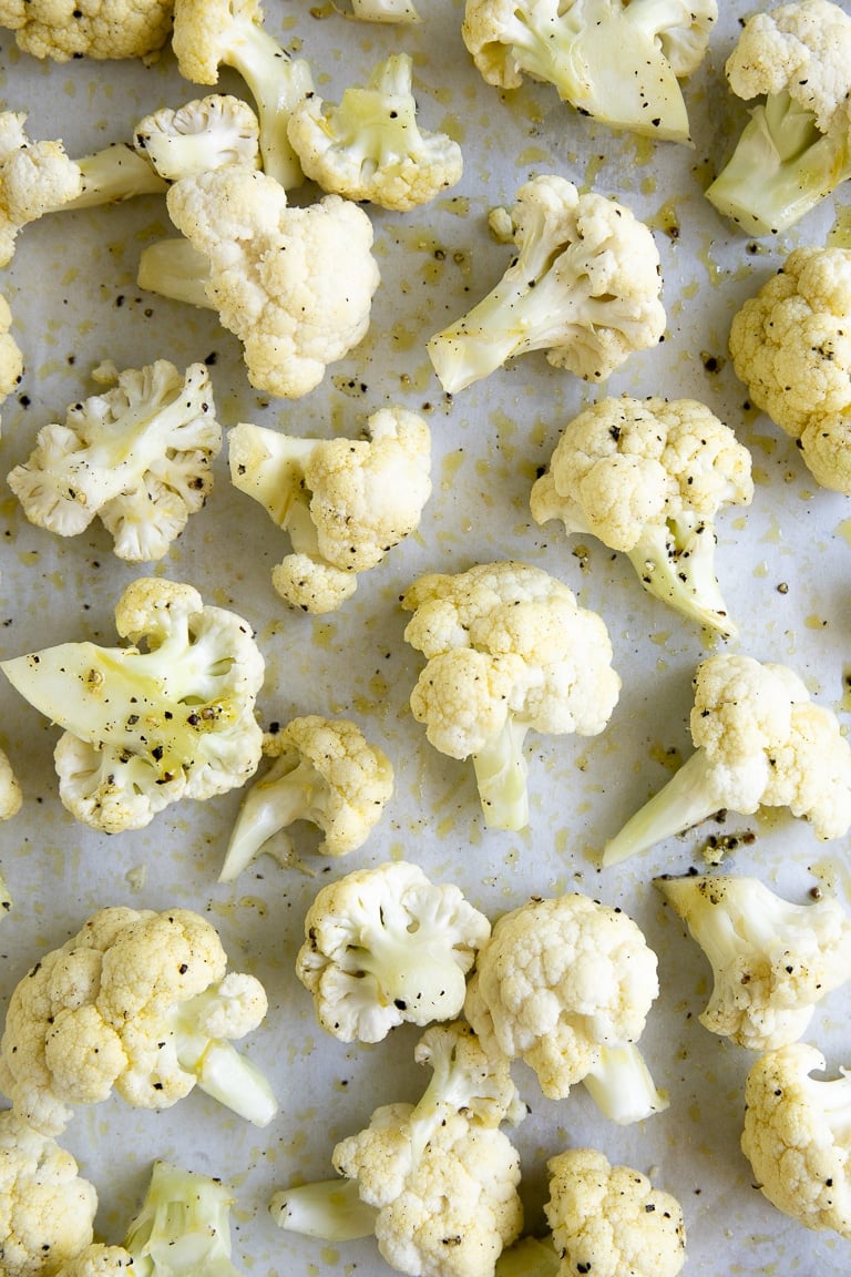 Cauliflower florets on a baking sheet tossed in olive oil, salt, and pepper.