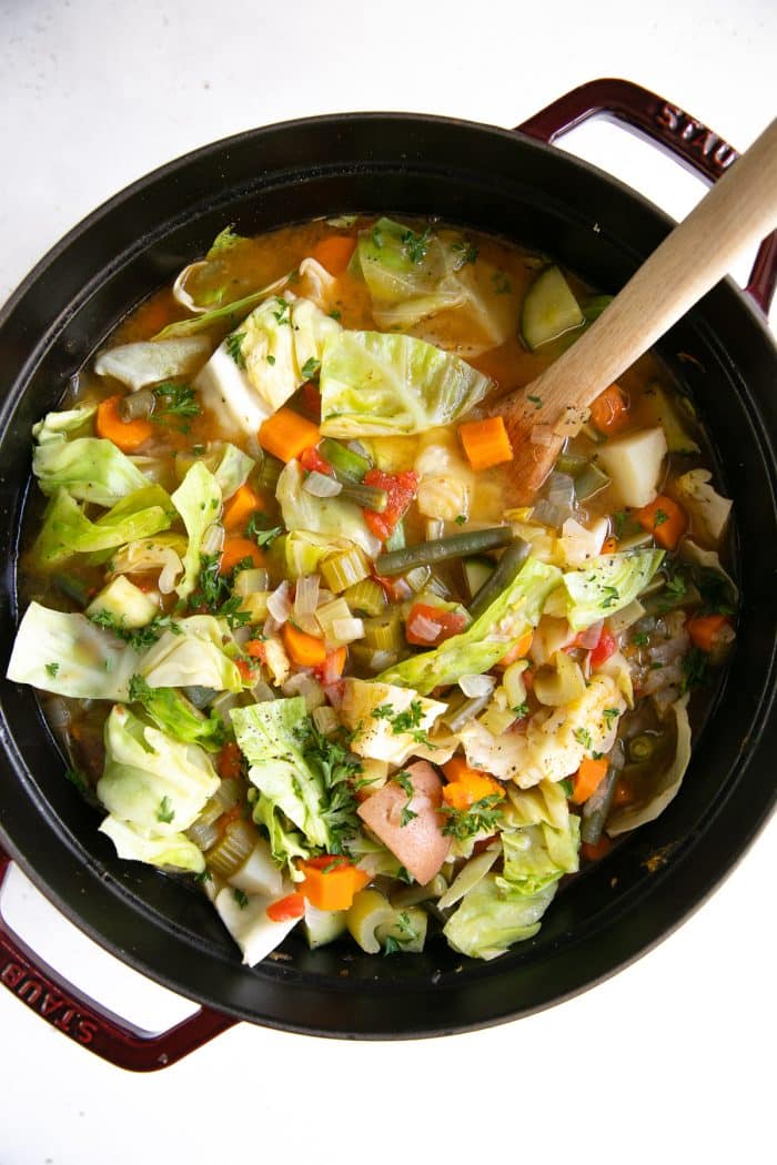 Large pot filled with homemade vegetable soup filled with cabbage, potatoes carrots, celery, and zucchini.