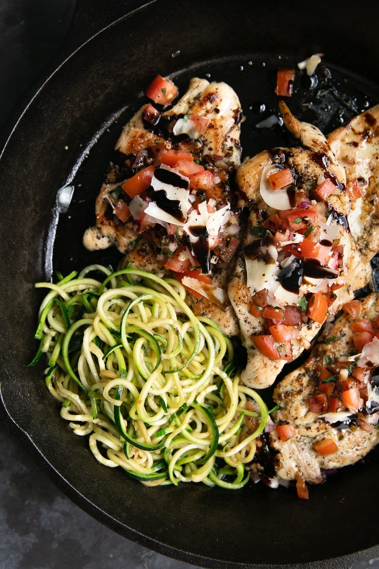 Cast iron skillet filled with cooked bruschetta chicken topped with tomatoes, balsamic glaze, and served with zucchini noodles.