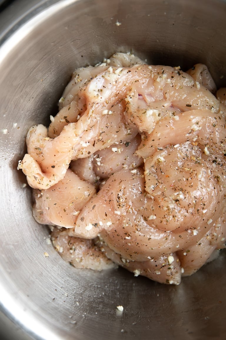 Mixing bowl filled with raw chicken breasts coated in olive oil and seasoning.
