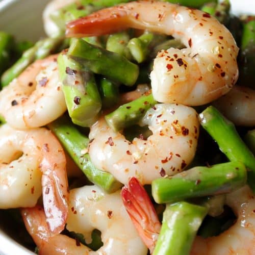 Zoomed in image of a white bowl filled with juicy shrimp and asparagus in lemon and garlic stir fry sauce.