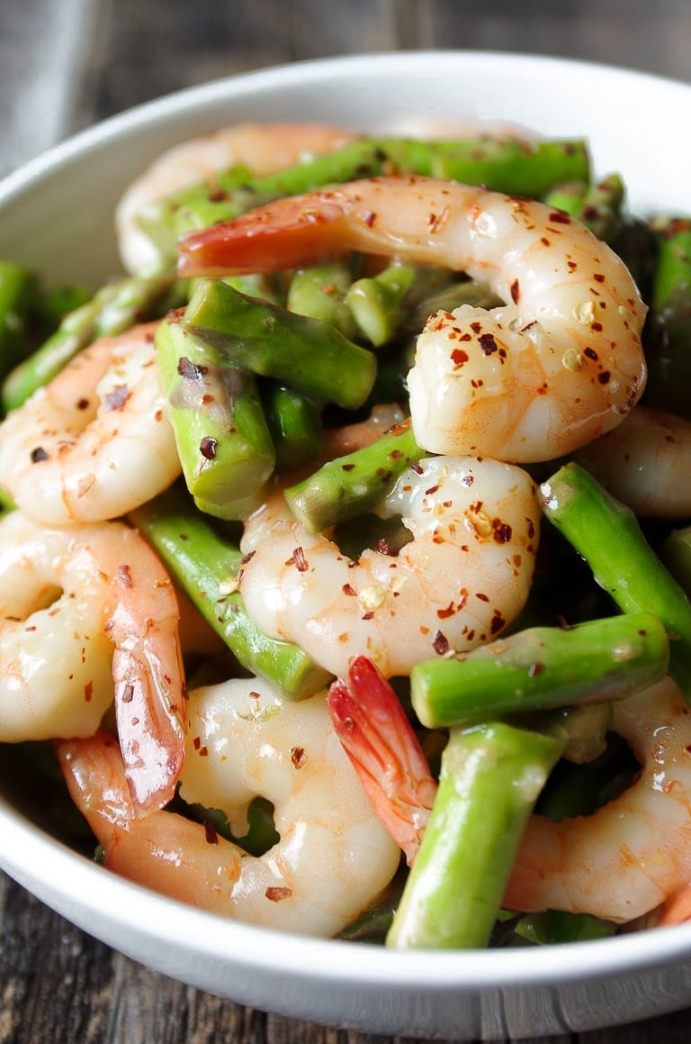 Zoomed in image of a white bowl filled with juicy shrimp and asparagus in lemon and garlic stir fry sauce.