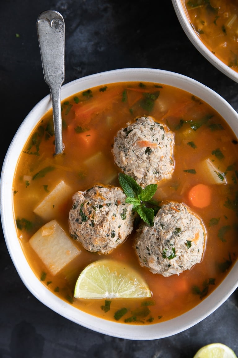 White bowl filled with albondigas soup and three albondigas meatballs.