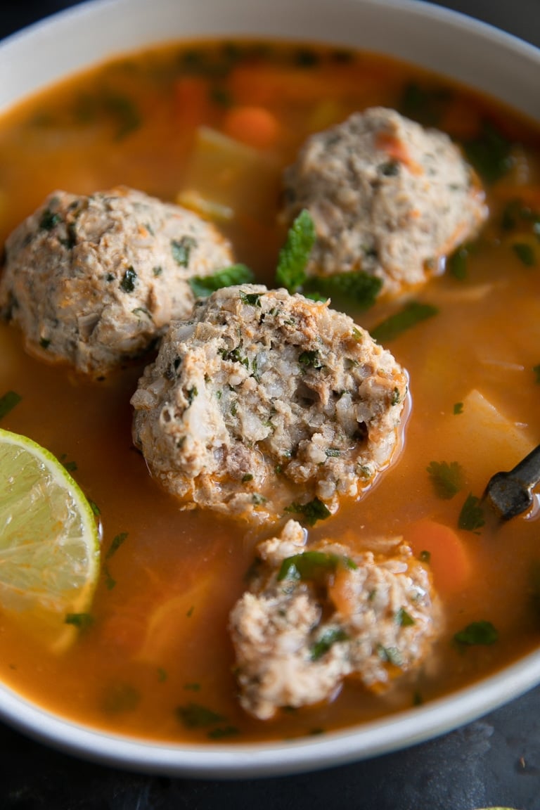 Bowl of albondigas soup garnished with mint leaves, cilantro, and lime.
