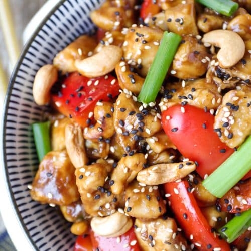 Close up image of cashew Chicken in a large blue and white serving bowl garnished with sesame seeds and green onions.