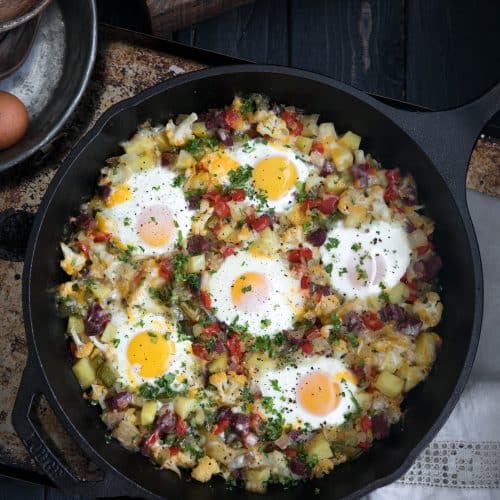 A skillet of corned beef potato egg hash on top of a wooden table
