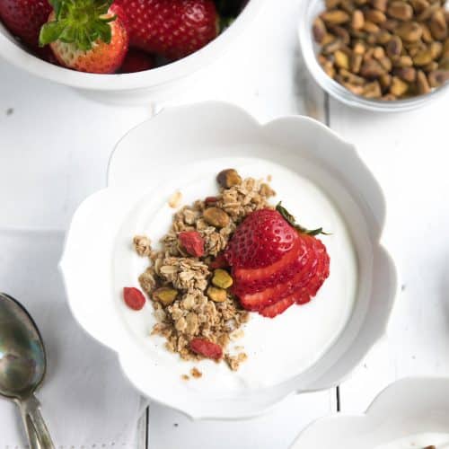 White bowl filled with plain greek yogurt and topped with homemade lightly sweetened granola.