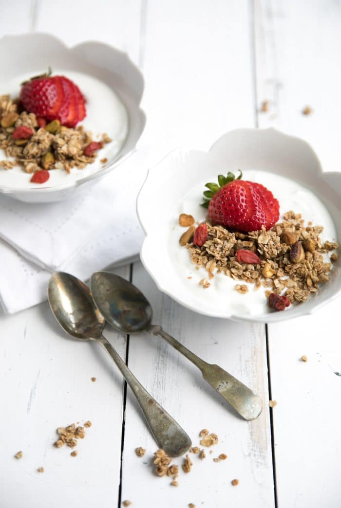 Two white bowls filled with plain greek yogurt and topped with homemade lightly sweetened granola.