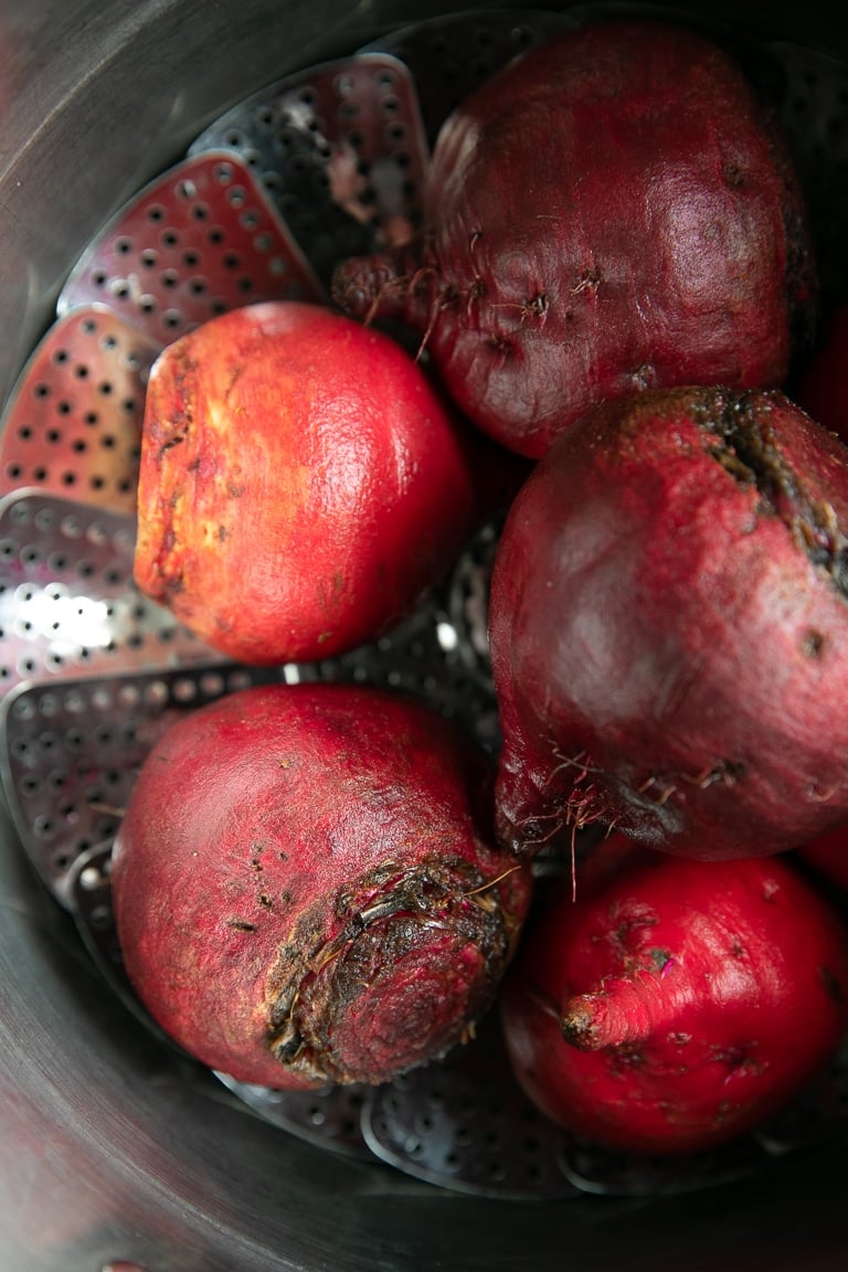 Raw beets in a large pot with a steaming basket.