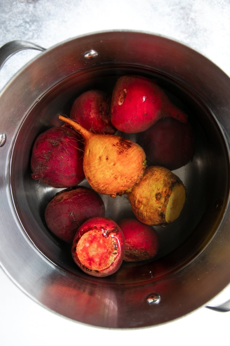 Raw beets in a large pot with a steaming basket.