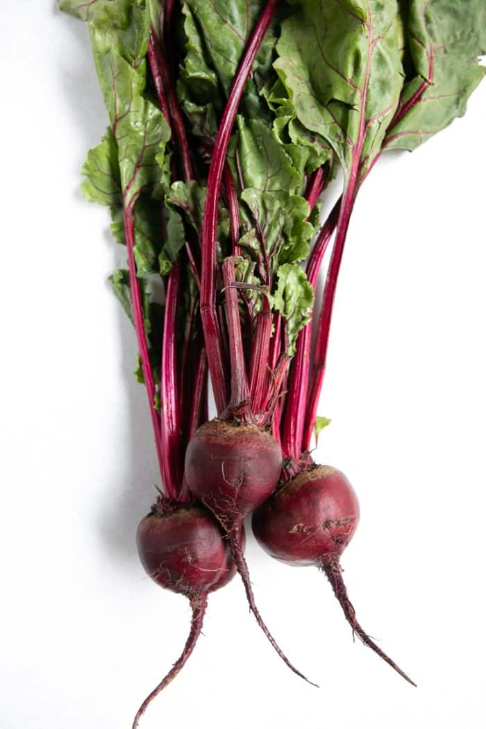Three raw beetroots with greens attached.