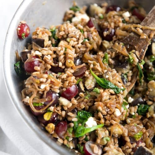 Large bowl filled with cooked farro, roasted eggplant, caramelized onions, grapes, feta cheese.