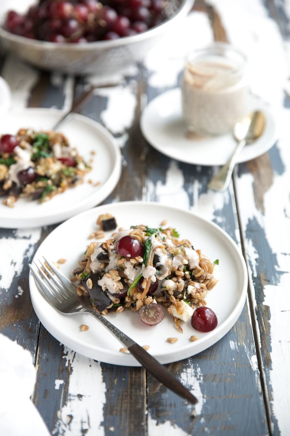 Serving plates with farro salad mixed with roasted eggplant, caramelized onions, grapes, feta cheese, and drizzled with walnut dijon dressing.