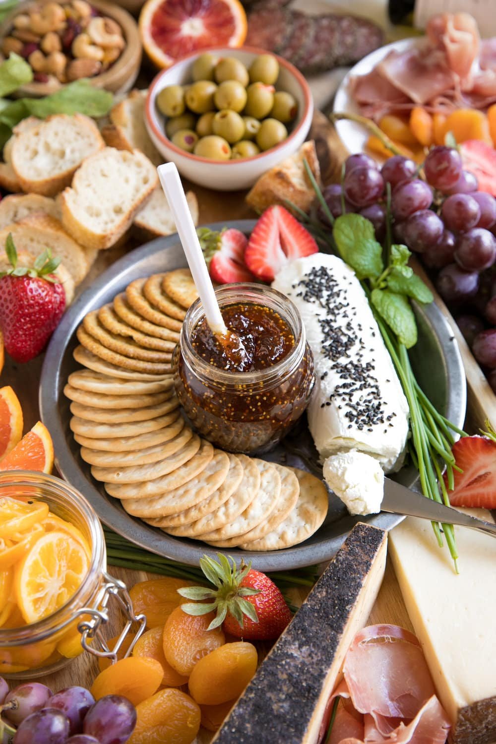 Spring Cheese Board with large assortment of meats cheese fruits and nuts with wine featuring fig jam in middle