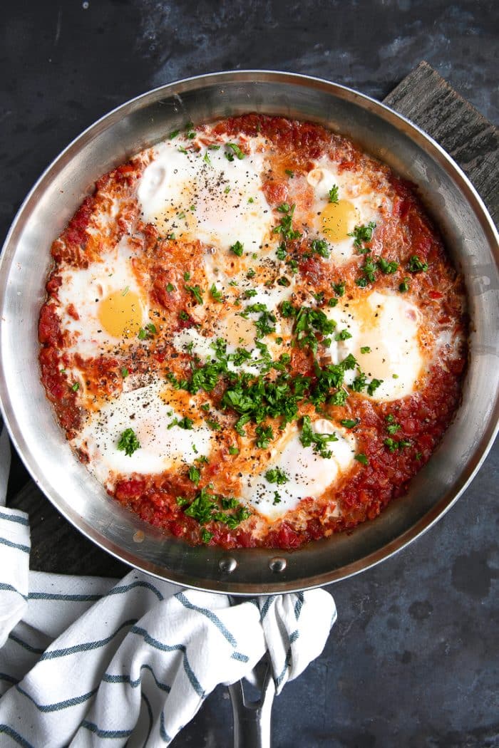 Skillet filled with tomato sauce and poached eggs garnished with chopped parsley.