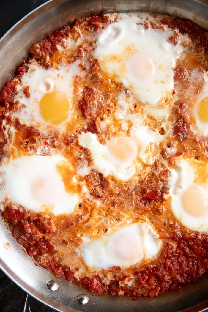 Shakshuka with 7 poached eggs in tomato sauce in a skillet.