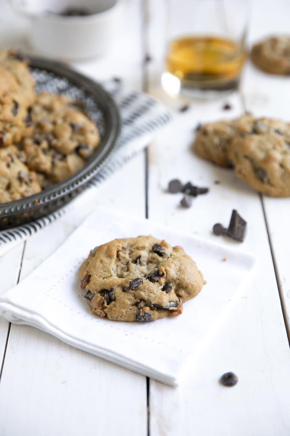 lightly browned cookie with chocolate chunks, and bacon. glass of bourbon in background