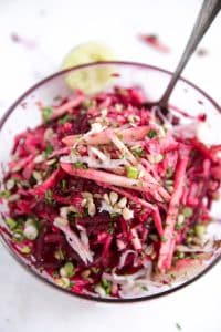 Glass bowl filled with raw beets, shredded kohlrabi, apples, green onion, feta, and sunflower seeds all mixed together.