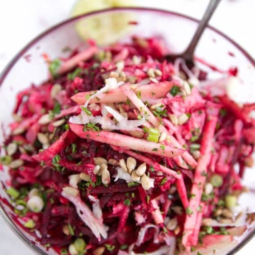 Glass bowl filled with raw beets, shredded kohlrabi, apples, green onion, feta, and sunflower seeds all mixed together.