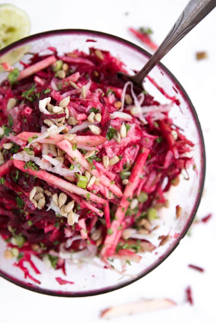 Glass bowl filled with raw beets, shredded kohlrabi, apples, green onion, feta, and sunflower seeds all mixed together. 