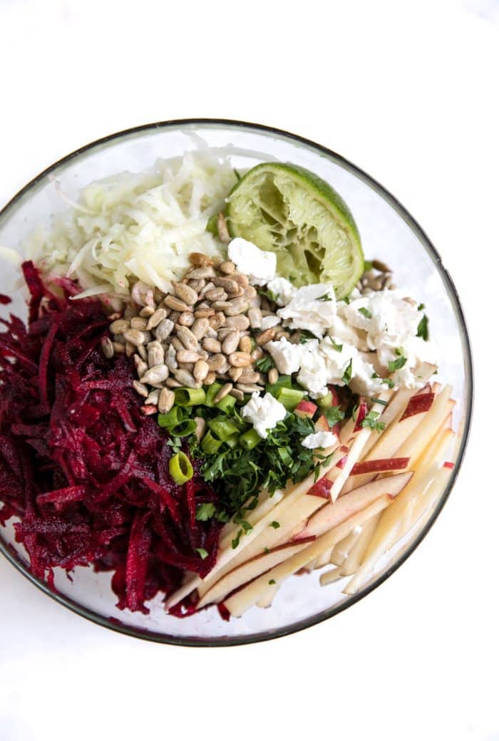 Glass bowl filled with with ingredients needed to make a beet and kohlrabi slaw with apples.