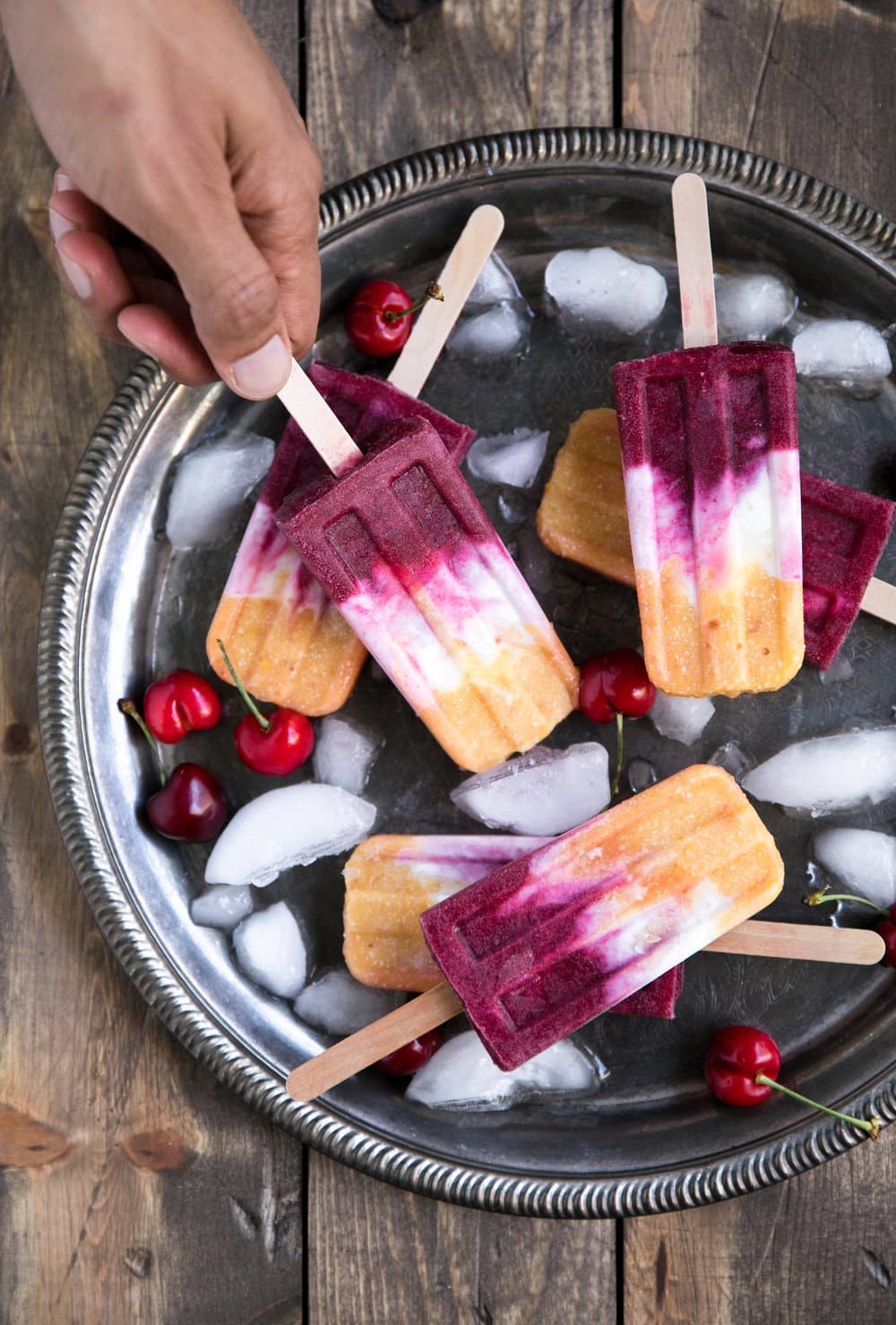 hand reaching for Roasted Peach and Cherry Coconut Popsicles