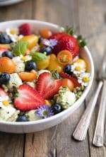 Large white bowl filled with farro tossed in homemade pesto and served mixed with fresh strawberries, blueberries, mozzarella cheese, and tomatoes.
