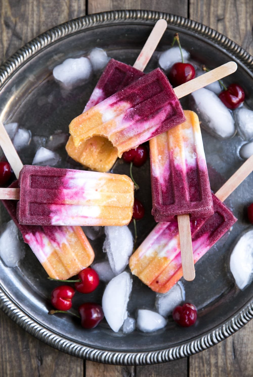 roasted peach and cherry coconut popsicles on a platter with ice and cherries