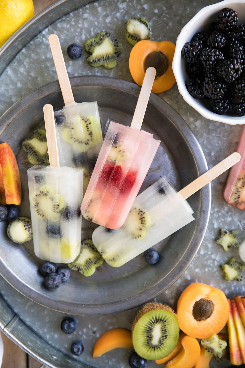 Homemade lemonade and fruit popsicles on a metal serving tray.