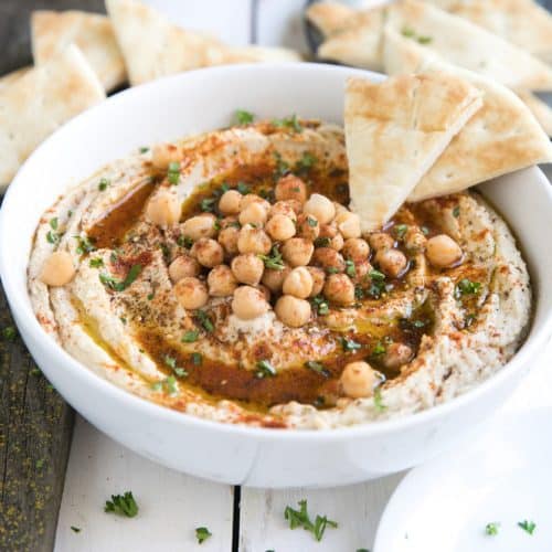 White bean hummus in a white bowl on a wooden white table served with pita bread.