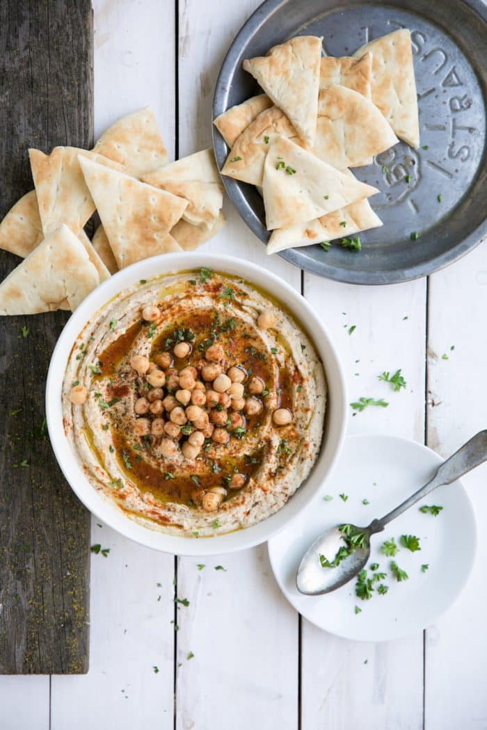 White bean hummus in a white bowl on a wooden white table served with pita bread.