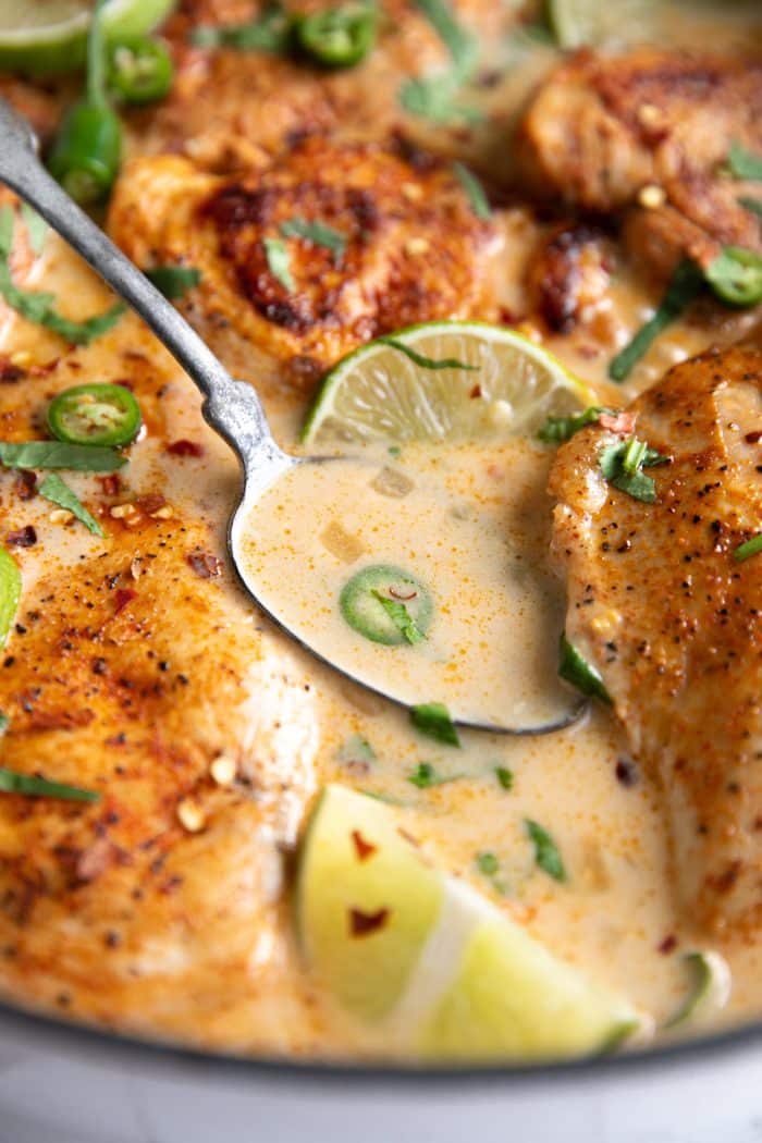 Spoon filled with cream sauce made with coconut milk and lime juice surrounded by simmering chicken breasts.