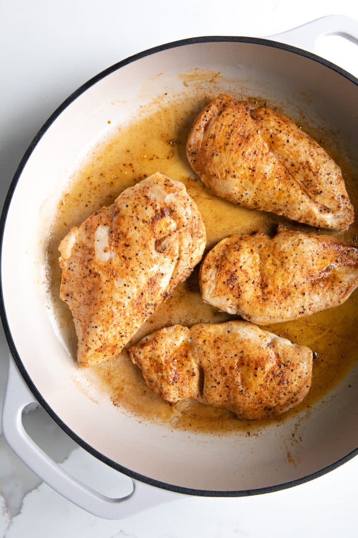 Large white enameled pan filled with four thinly sliced and seared chicken breasts seasoned with salt, pepper, and paprika.