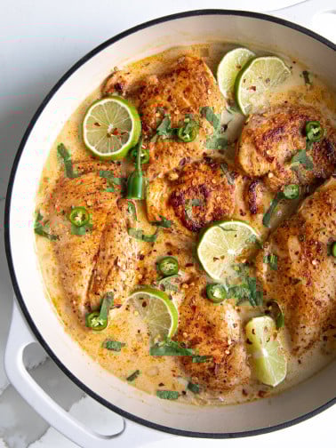 Large white enameled skillet filled with thinly sliced chicken breasts simmering in a homemade sauce made with coconut milk, chicken broth, and lime juice, and garnished with lime slices and fresh cilantro.
