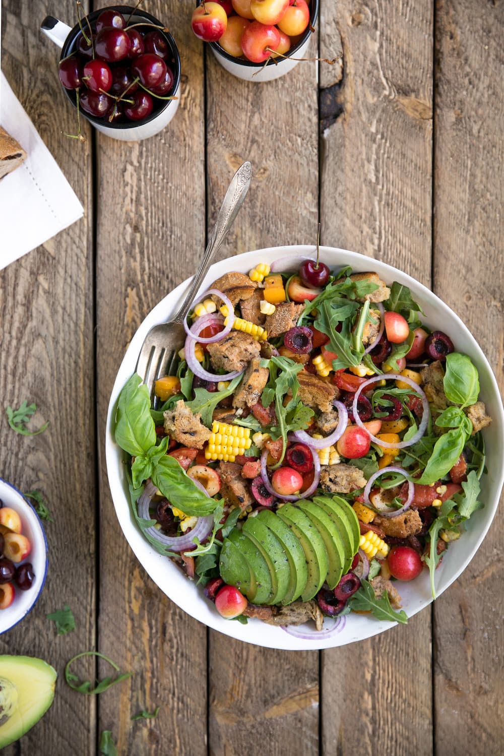 overhead photo of large bowl of Cherry and Rocket Panzanella Salad with two side dishes of cherries