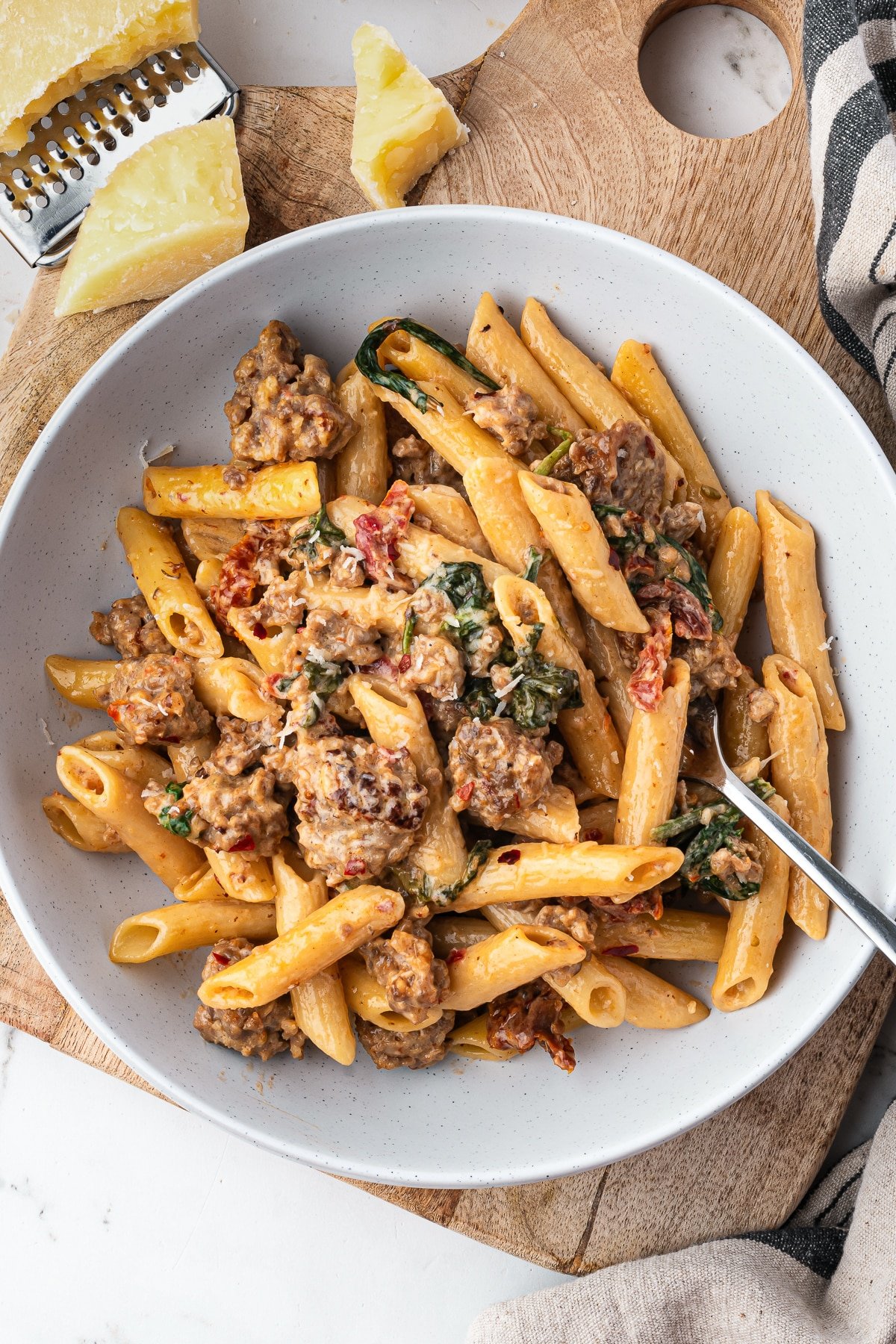 Overhead view of creamy sausage pasta in a bowl with Parmesan cheese wedges on the side.